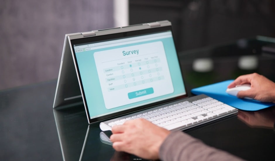 Person completing an online survey on a laptop in tent mode with a wireless keyboard and mouse.